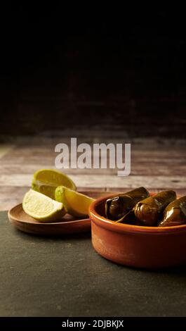 Dolmades stuffed vine leaves ready to eat. in a terracotta dish with lime wedges on a wooden table. Stock Photo