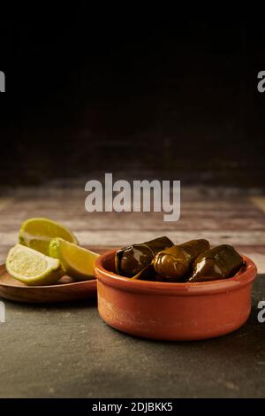 Dolmades stuffed vine leaves ready to eat. in a terracotta dish with lime wedges on a wooden table. Stock Photo