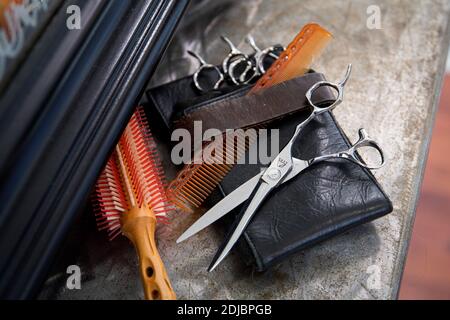 Hairdressing professional tools: comb, hairbrush, scissors and leather case displayed on a shelf in front of the mirror Stock Photo