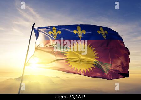 Guadeloupe flag waving on the top sunrise mist fog Stock Photo