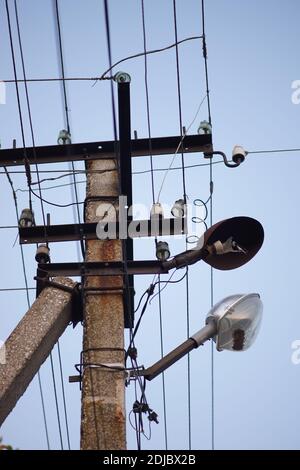 old stone pillar with wires and broken lamp on the blue sky background. Stock Photo