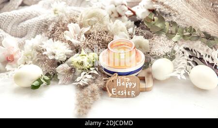 Spring still life with Easter eggs, burning candles in a pendant and flowers against the background of decor details. Easter holiday concept. Stock Photo