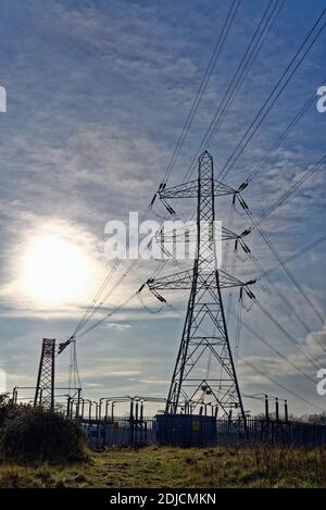 National grid pylon against a blue sky and a flaring sun, Byfleet Surrey England UK Stock Photo