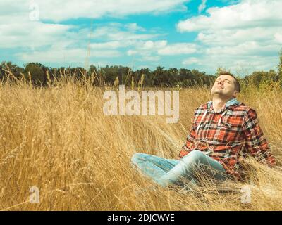 Young man relaxes sitting in nature in grass in autumn. Stock Photo