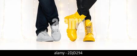 Banner made with unrecognizable people in bright yellow boots and sneakers standing against white wall with fairy lights Stock Photo