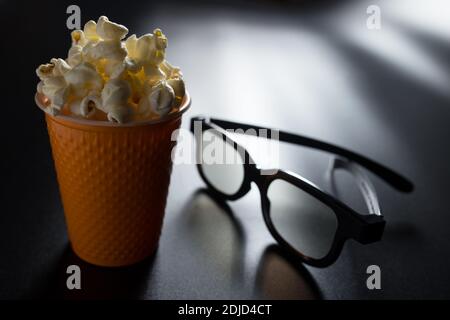 Watching a 3D movie at home with popcorn. bucket of popcorn and 3D glasses on black background. Stock Photo