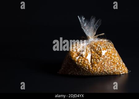 Seeds of popcorn in plastic bag, on blacl background with copyspace. Stock Photo