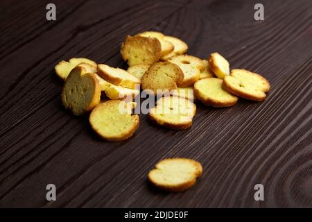 Bruschette chips, dry slices of baked bread, beer snacks. Heap of bruschette chips scattered on brown wooden table Stock Photo