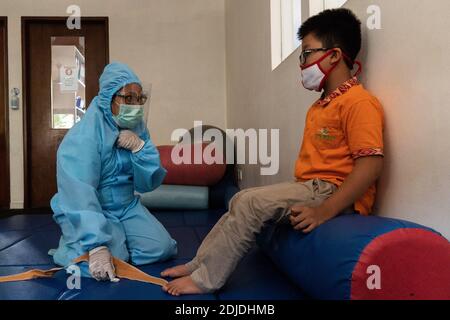 BALI/INDONESIA-OCT 23 2020: a child with a physical disability is doing physical therapy. They wear masks and hamzat suit to avoid the spread of the C Stock Photo