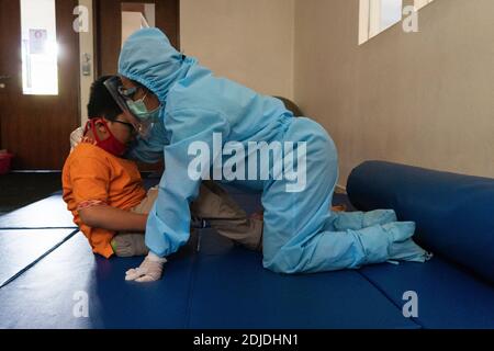 BALI/INDONESIA-OCT 23 2020: a child with a physical disability is doing physical therapy. They wear masks and hamzat suit to avoid the spread of the C Stock Photo