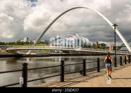 Female runner along River Tyne, Gateshead Millennium Bridge and The Sage Gateshead concert hall, Quayside, Newcastle, Northumberland, England