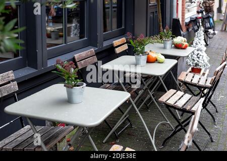 Street cafe during Christmas with pumpkins and Red Skimmia flowers European style. Outdoor tables with chairs on cafe terrace in Amsterdam. Vintage Stock Photo