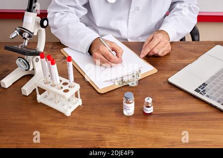 close-up photo of doctor's male making notes, writing results, using test tubes of covid-19. laptop, tubes on table Stock Photo