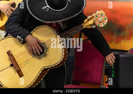 Selective focus of hands of young man mariachi, holding and playing acoustic bass guitar with orchestra and ajusting volume during the festival of dia de los muertos Stock Photo