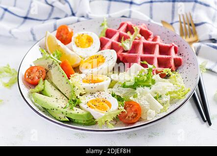 Breakfast with beetroot waffles, boiled egg, tomato and slice avocado on white background. Appetizers, snack, brunch. Healthy food. Stock Photo