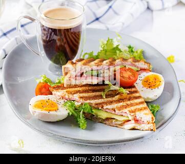 Grilled club sandwich panini with ham, tomato, cheese, avocado and cup of coffee. Delicious breakfast or snack. Stock Photo