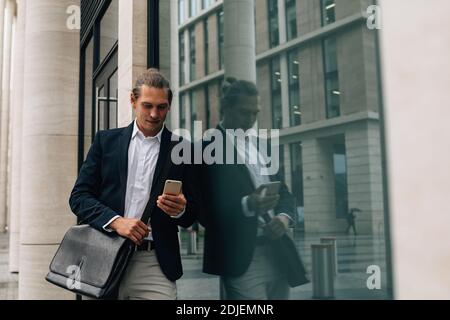 Businessman in formal wear looking on smartphone standing at office building Stock Photo