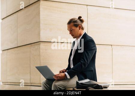 Young businessman sitting with laptop computer on his hips. Man in formal wear working outdoors. Stock Photo