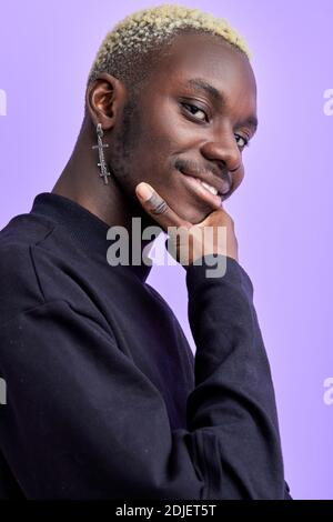 black guy in casual black wear looks at camera touching the chin, smiling isolated over purple background Stock Photo