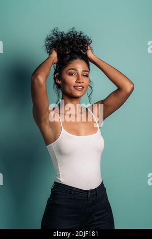 Stock photo of young and cheerful woman smiling and looking at camera in studio shot. She is playing with her curly hair. Stock Photo