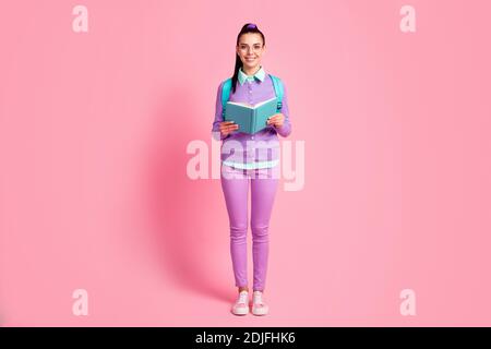 Full length photo of young lady hold book look camera wear specs bag violet pullover pants sneakers isolated pink color background Stock Photo