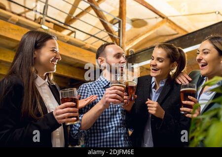 Having fun. Happy co-workers celebrating corporate event after tensioned work day. Look delighted, friendly, cheerful. Drinking beer. Concept of office culture, teamwork, friendship, holidays, weekend. Stock Photo