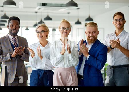 portrait of successful multi-ethnic team looking at camera in the office, posing, young people have a good cooperation, stand clapping hands celebrati Stock Photo