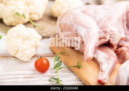 Whole raw rabbit with cauliflower, tomatoes and spices on a white wooden background and linen textile. Side view, close up, selective focus. Stock Photo