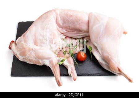 Whole raw rabbit with tomatoes, pea sprouts on a black concrete slate board isolated on white background. Side view, close up. Stock Photo