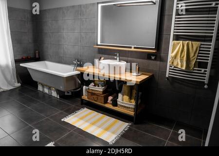 Bathroom in a concrete style with a bath, sink and big mirror. Stock Photo