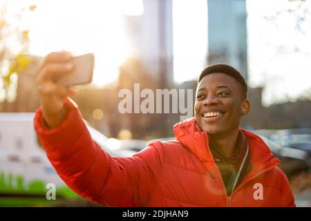 Young man smiles while video chatting with friend on smartphone outdoors Stock Photo