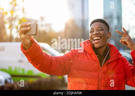 Young man smiles while video chatting with friend on smartphone outdoors Stock Photo