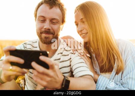 Image of a young happy positive loving couple using mobile phone outside at the field Stock Photo