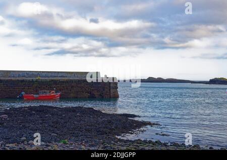 A small wooden Fishing boat with a reed hull moored up alongside the traditional old stone Quay at Catterline, on the East Coast of Scotland. Stock Photo