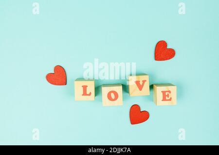Red hearts and wooden cubes with text LOVE on blue background. Creative flat lay with copy space. Festive greeting card for St Valentines day Stock Photo