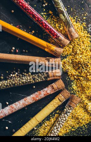 A set of spices in small jars with cork lids. Pink salt, ginger, turmeric, masala, paprika, smoked paprika. Spices on a black surface. Stock Photo