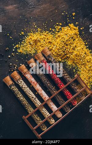 A set of spices in small jars with cork lids. Pink salt, ginger, turmeric, masala, paprika, smoked paprika. Spices on a black surface. Stock Photo