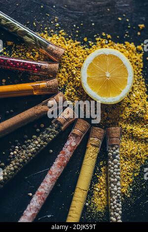 A set of spices in small jars with cork lids. Pink salt, ginger, turmeric, masala, paprika, smoked paprika. Spices on a black surface. Stock Photo