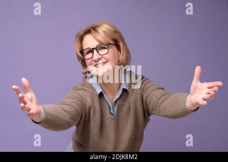 Cheerful european mature woman welcoming you with her arms outstretched out. Studio shot Stock Photo