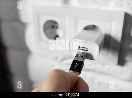 Unplugging USB cable from power adapter. Disconnect USB cord from the cellphone charger. Man hold USB plug against wall charger. Plug-in connector Stock Photo