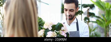 Handsome young man giving flower to lady in plant store Stock Photo