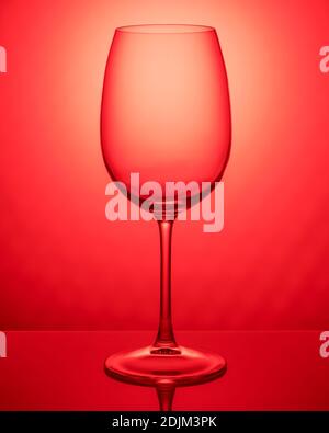 Transparent empty wineglass on the red background. Object photography. Stock Photo