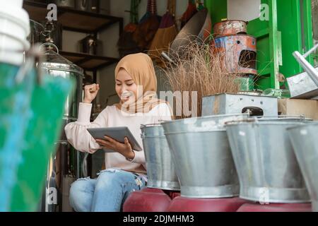 joy of female seller using tablet with raise hand when surprised in the household appliances store Stock Photo