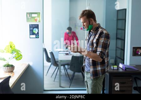 Caucasian man wearing face mask using smartphone in office Stock Photo