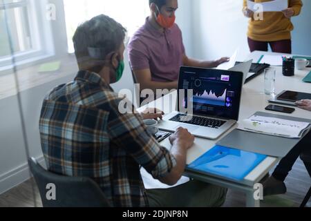 Diverse group of colleagues wearing face masks working at desk in office Stock Photo