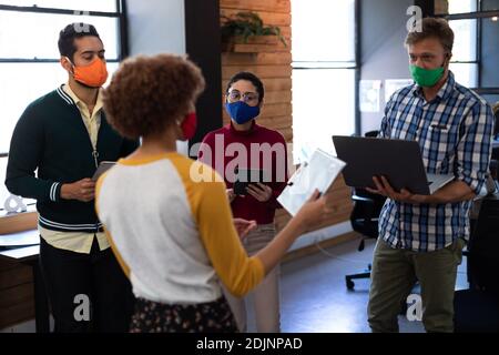 Diverse group of creative colleagues wearing masks having discussion in office Stock Photo