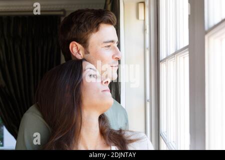 Caucasian couple looking out of window smiling woman leaning on man Stock Photo