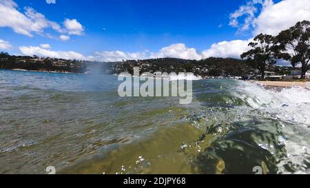 HOBART, TASMANIA - December 6th, 2020: waves crashing at the beach in the popular suburb of Kingston Beach in Suthern Tasmania on a sunny summer day Stock Photo