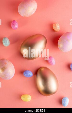 Trendy Easter background with Gold and colored Easter eggs on a light coral color background with copy space for text. Top view flat lay still life. E Stock Photo