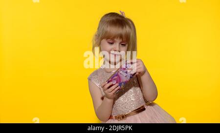 Little girl using smartphone. Portrait of child texting on smartphone. Kid enthusiastically playing games on mobile phone isolated on yellow background in studio. Technology for children Stock Photo